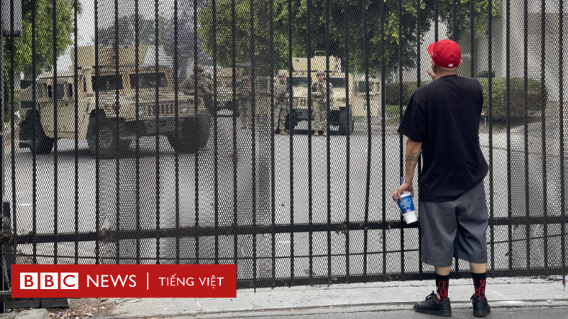 Một người phụ nữ và một người đàn ông đang ngồi đối diện nhau tại một bàn làm việc, cả hai đều đang xem xét một tài liệu giấy lớn với biểu đồ và văn bản. Họ trông nghiêm túc, tập trung và có vẻ đang thảo luận về các điều khoản trong hợp đồng hoặc quy định công việc.