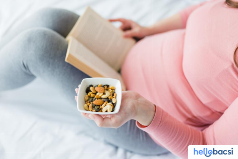 Hình ảnh mẹ bầu khỏe mạnh, rạng rỡ bên đĩa trái cây tươi ngon, đa dạng bao gồm chuối, cam, bơ, xoài và đu đủ chín. 